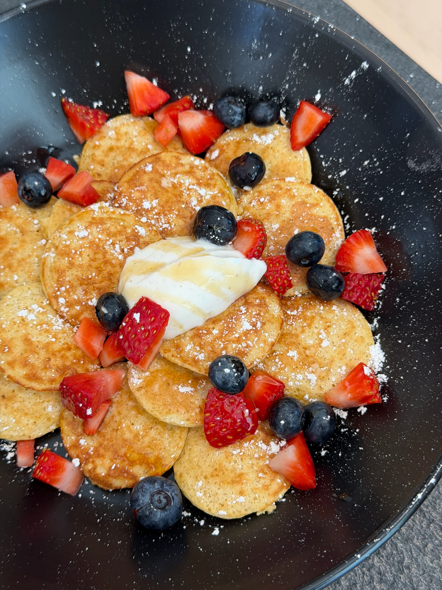 mini dutch pancakes topped with berries, powdered sugar, and yogurt